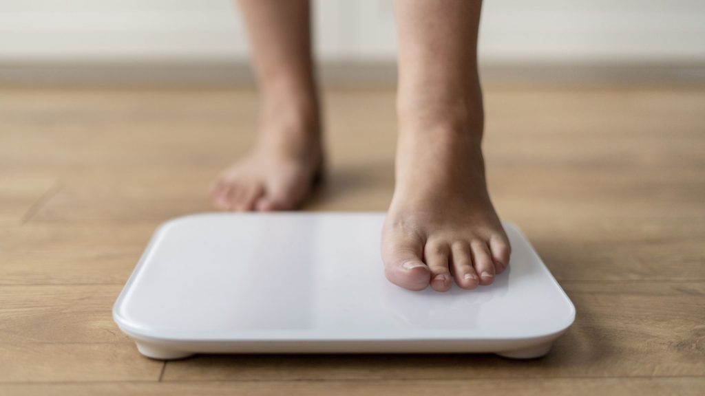 Picior care urcă pe un cântar, simbolizând obezitatea și creșterea în greutate influențată de factori hormonali și metabolici