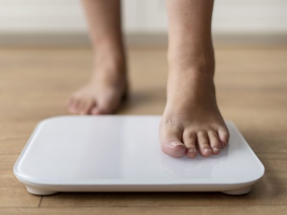 Picior care urcă pe un cântar, simbolizând obezitatea și creșterea în greutate influențată de factori hormonali și metabolici